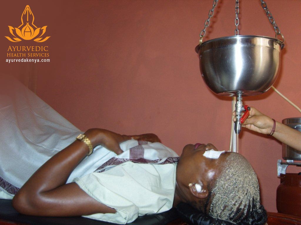 Warm oil poured in a steady stream onto a patient’s forehead during Shirodhara